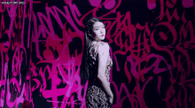 a woman stands in front of a wall with graffiti on it