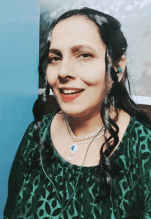 a woman wearing a green top and a pearl necklace is smiling