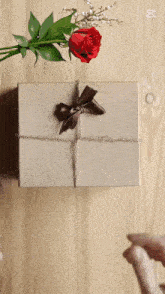 a box with a bow and a red rose on a wooden table