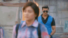 a man in a blue vest walks past a woman in a pink shirt