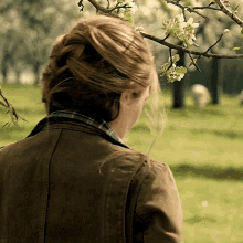 a woman in a brown jacket looks at a tree branch with flowers on it