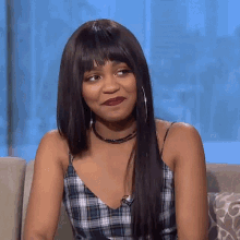 a woman is sitting on a couch wearing a plaid top