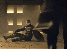 a man in a superhero costume is laying on the ground with a shield