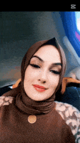 a woman wearing a hijab and a flower of life necklace smiles