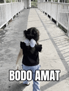 a little girl is walking across a bridge with bodo amat written on the sidewalk