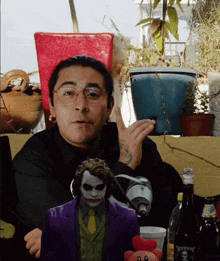 a man wearing glasses and a joker mask is sitting in front of a table with bottles and plants