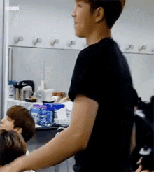 a man in a black shirt is standing in front of a group of people in a room .