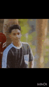 a boy wearing a shirt that says ' nk ' on it is standing next to a tree