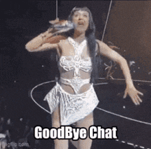 a woman in a white dress is singing into a microphone while dancing on a stage and says goodbye chat .