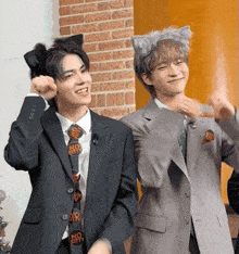 a man wearing a cat ear headband stands next to another man wearing a no kitty tie