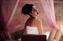 a woman is sitting on a bed under a pink canopy with a laptop .