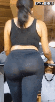 a woman in a black tank top and leggings is walking on a treadmill in a gym .