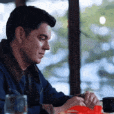 a man in a blue jacket sits at a table with a red bow