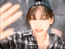 a young woman wearing a plaid shirt and a hat is waving her hand .