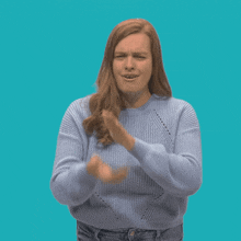 a woman wearing a blue sweater is clapping her hands in front of a blue background