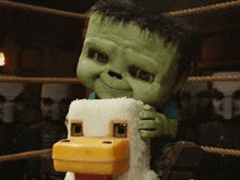 a green cartoon character is holding a stuffed animal in a boxing ring .