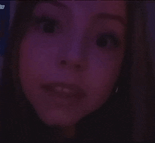 a close up of a woman 's face in a dark room with purple lights .