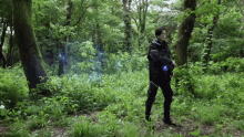 a man is walking through a lush green forest holding a blue object