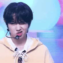 a boy wearing a yellow hoodie and a microphone making a funny face