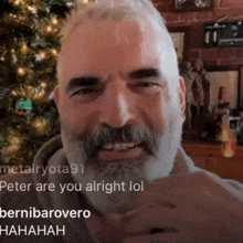 a man with a beard is smiling in front of a christmas tree while someone says " better are you alright lol "
