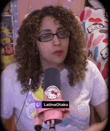 a woman wearing glasses and a hello kitty shirt is talking into a pink microphone