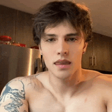 a shirtless man with a tattoo on his arm is looking at the camera .