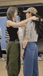 two women standing next to each other with one wearing a black tank top that says ' 3 story ' on it