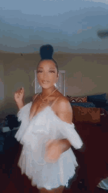 a woman in a white dress is dancing in a living room with a bun in her hair .