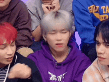 a group of young men are sitting in a row and one of them is wearing a purple sweatshirt .