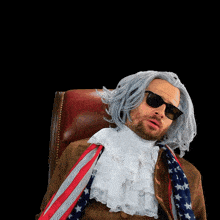 a man wearing a wig and sunglasses sitting in a chair