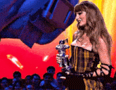 a woman in a plaid dress is holding a trophy on a stage in front of a crowd .