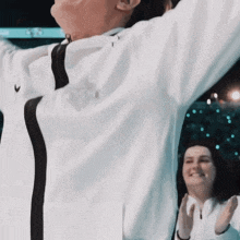 a man in a white nike jacket stands in front of a woman clapping