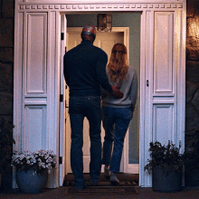 a man and a woman are standing in a doorway with a potted plant in front of them