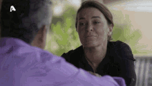 a woman in a black shirt is talking to a man in a purple shirt with the letter a in the corner .