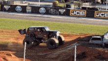 a monster truck is driving on a dirt track in front of a jcb advertisement