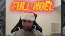 a man wearing a santa hat is sitting in front of a sign that reads full noel