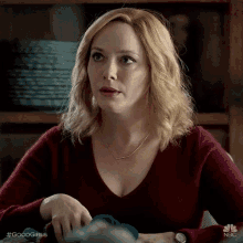 a woman in a red sweater is sitting at a table with her hands on her hips .