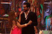 a man in a suit and a woman in a red dress are dancing in a room with jiocinema written on the bottom