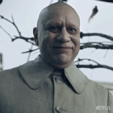a bald man is smiling in front of a tree with a netflix logo in the corner