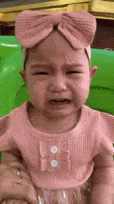 a baby wearing a pink headband and a pink shirt is crying