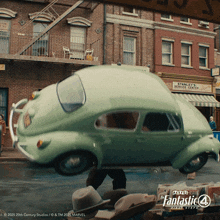 a green car is driving down a street in front of a brick building that says stanley schroder