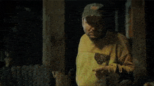 a man in a yellow shirt and hat is standing in a dark room holding a lighter .
