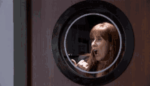 a woman with red hair looks through a round window
