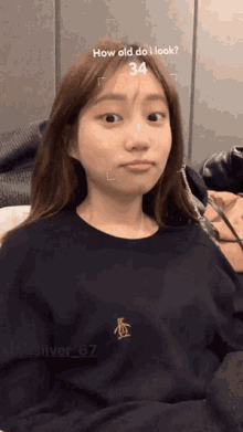 a woman wearing a black shirt with a gold penguin on it is being asked how old she is