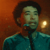 a man singing into a microphone wearing a necklace with the letter g on it