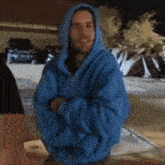 a man in a blue hoodie stands with his arms crossed in front of tents