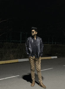 a man wearing sunglasses and a leather jacket stands on a street