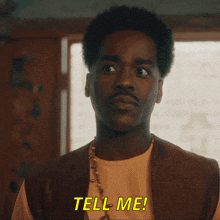 a man in an orange shirt says tell me in yellow letters