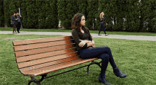 a woman sits on a wooden park bench