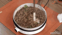 a pan of ground meat is being stirred with a wooden spoon and the words made in animatica are visible